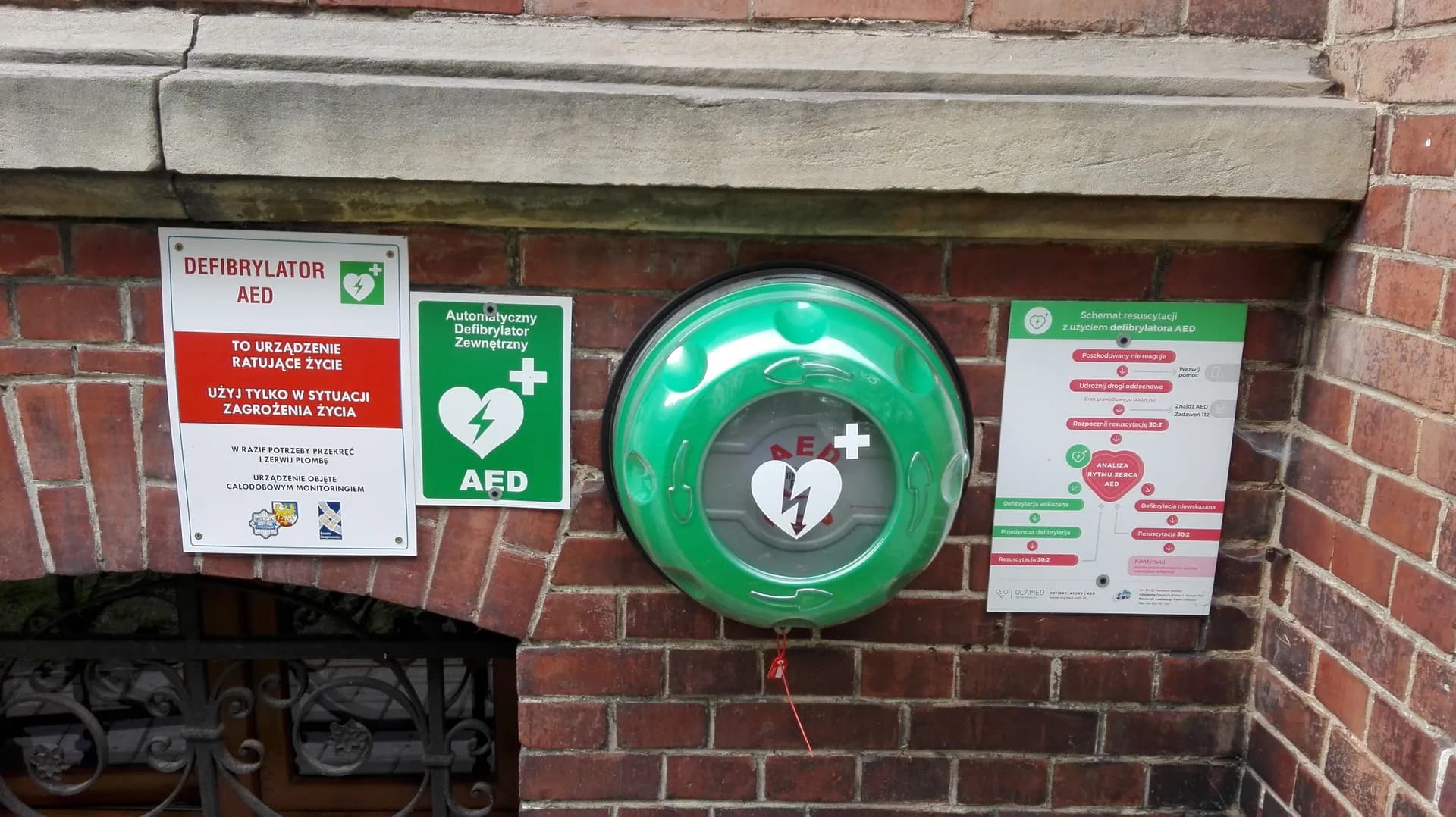 Defibrylator AED zamontowany na ceglanej ścianie budynku Zespołu Szkół Ogólnokształcących nr 1 w Prudniku