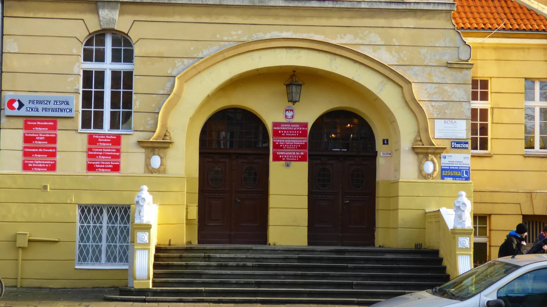 Wejście do budynku przy ul. Staszica 4 w Bydgoszczy z tablicami informacyjnymi placówek edukacyjnych