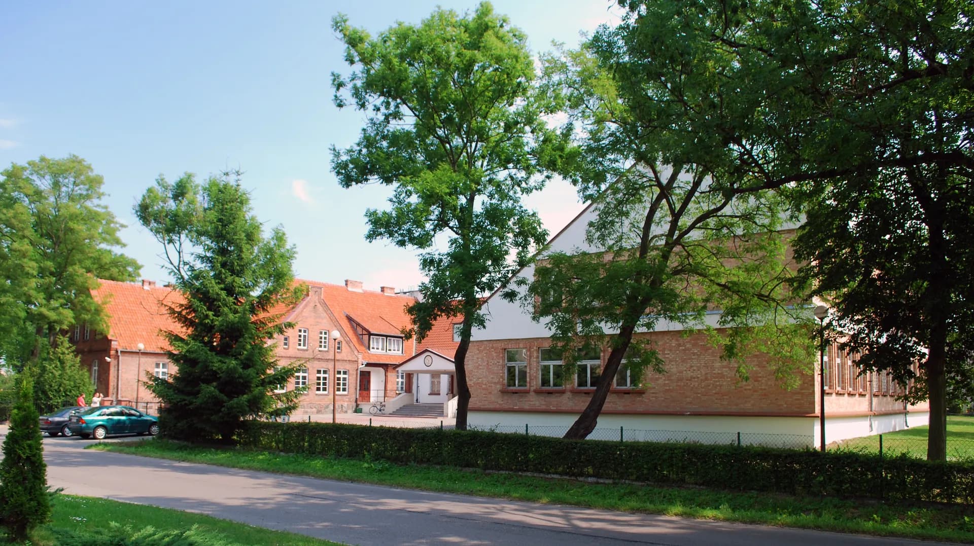 Budynek Zespołu Szkół w Ostaszewie widziany zza drzew i ulicy