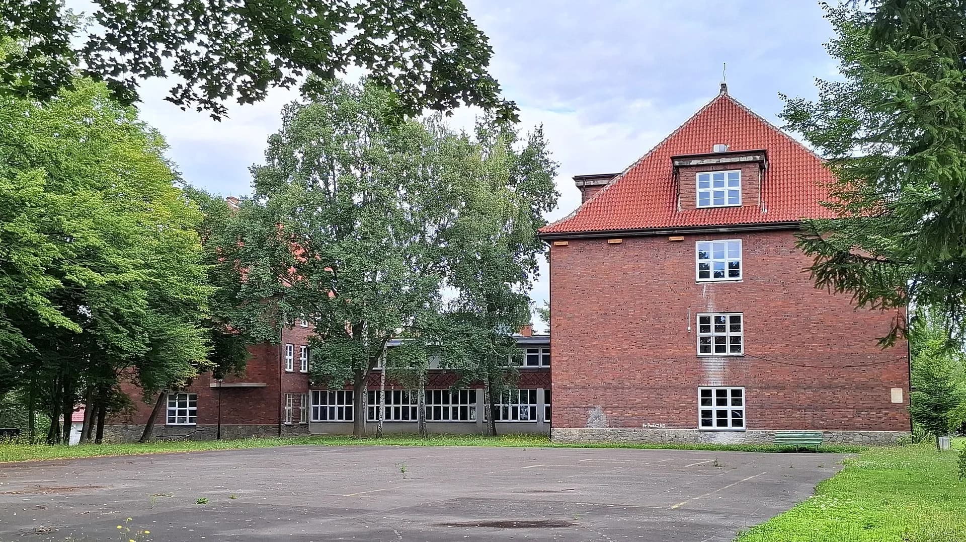 Ceglany budynek II Liceum Ogólnokształcącego w Prudniku widziany od strony placu i zieleni