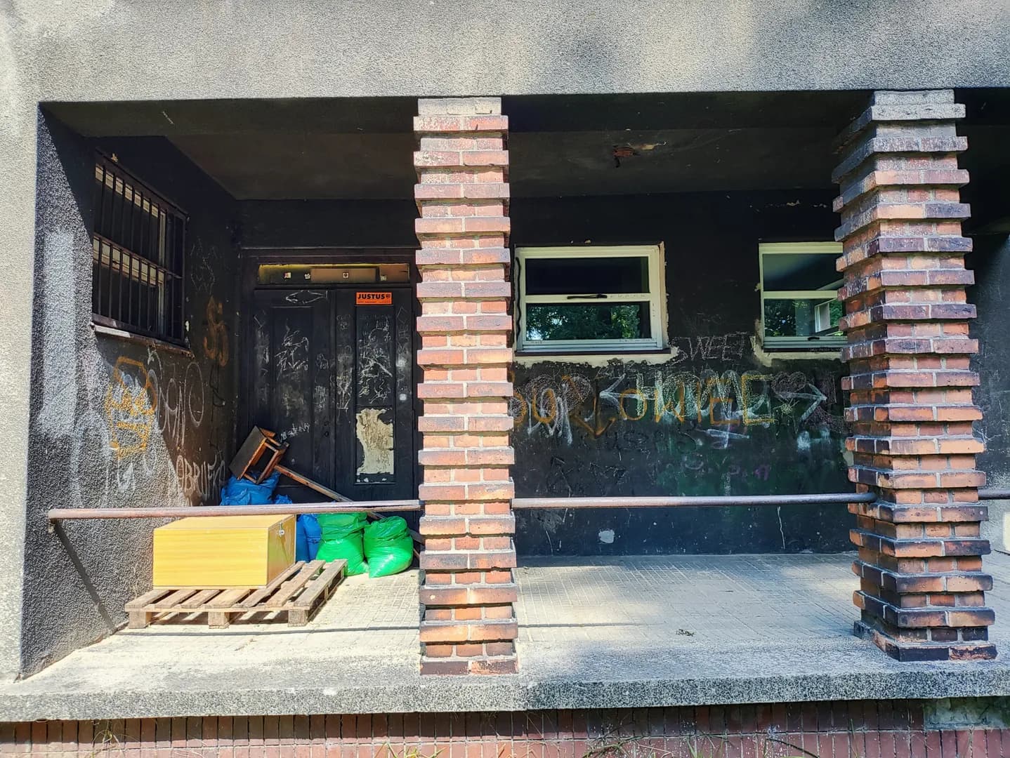 Zniszczone wejście do budynku przedszkola z ceglanymi filarami i graffiti