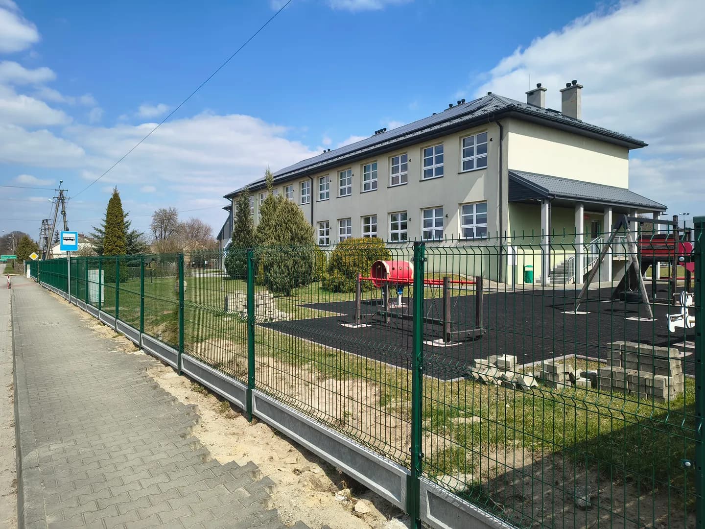Budynek i plac zabaw Szkoły Podstawowej w Chorzewie widziane zza ogrodzenia