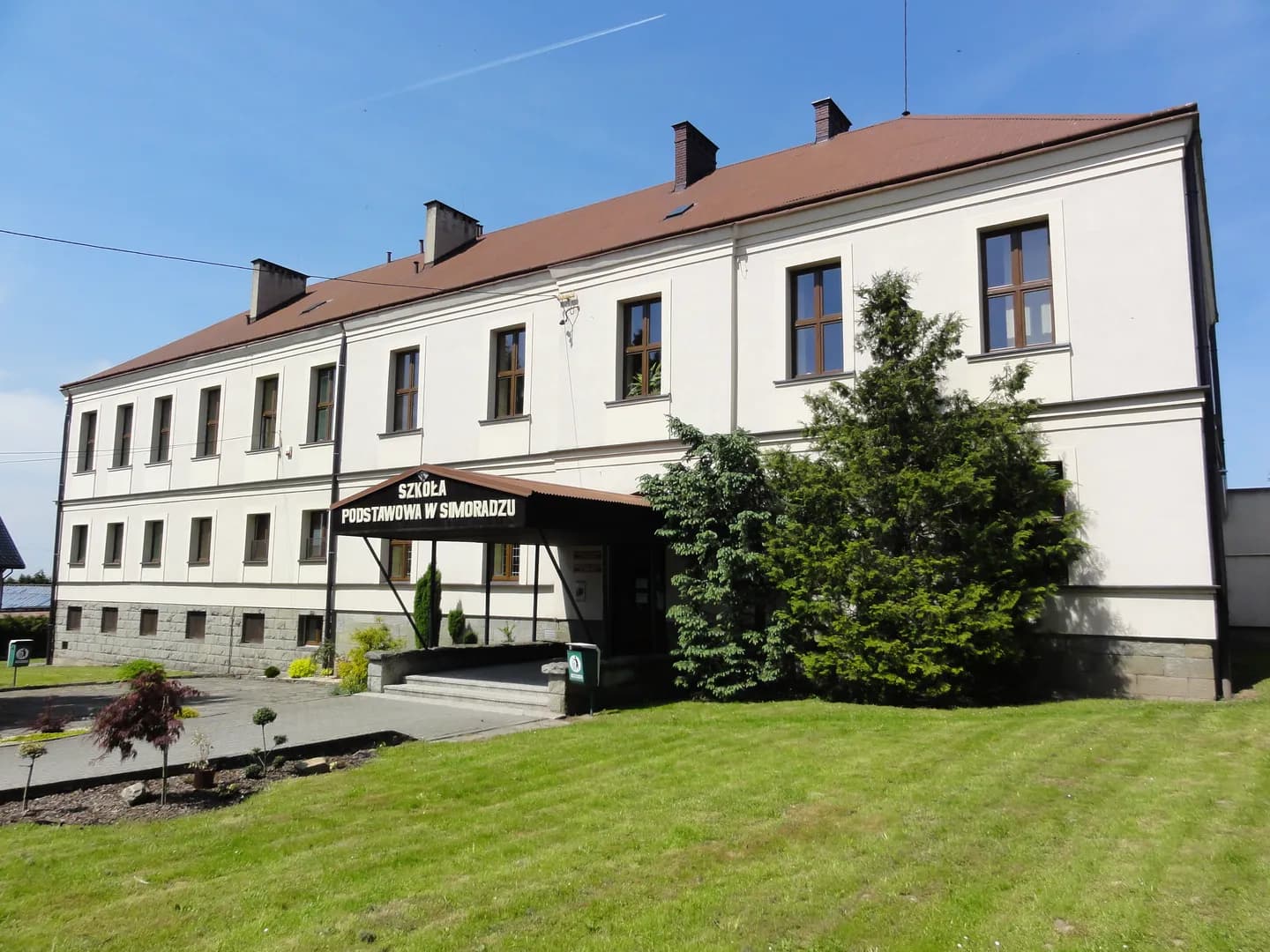 Elewacja frontowa Szkoły Podstawowej w Simoradzu z widocznym wejściem i trawnikiem