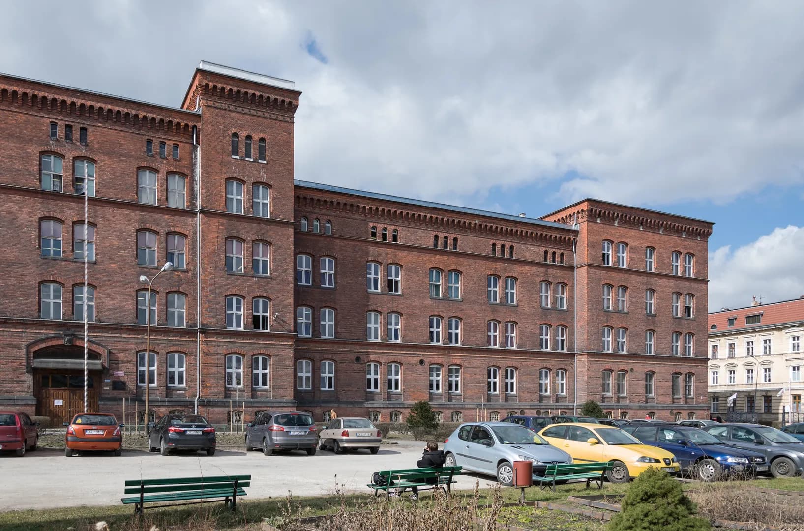 Ceglany budynek szkoły w Kłodzku z parkingiem z przodu