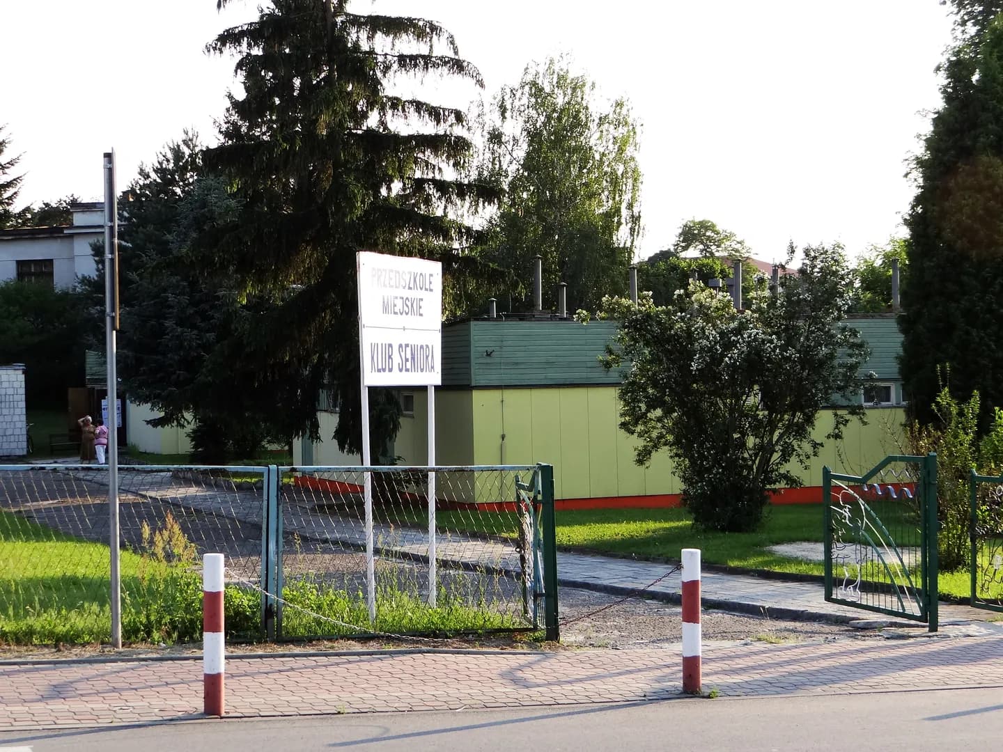 Teren i budynek Przedszkola Miejskiego w Rudniku nad Sanem widziany zza ogrodzenia z tablicą informacyjną