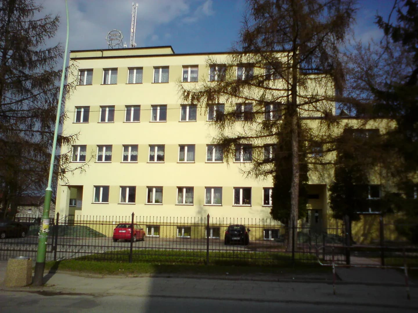 Elewacja budynku szkoły z ogrodzeniem i drzewami od frontu