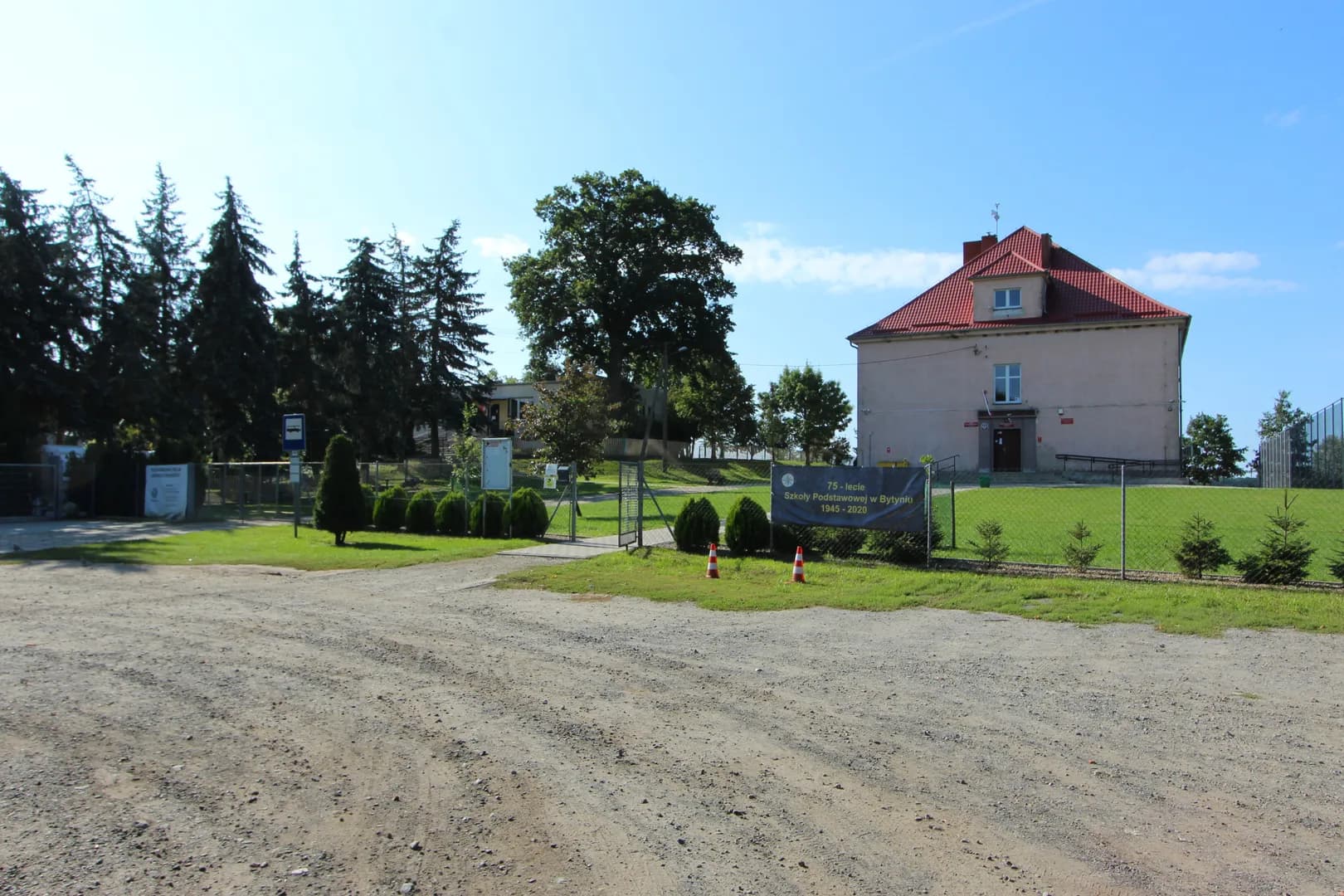 Widok na budynek Szkoły Podstawowej w Bytyniu z placem i ogrodzeniem.