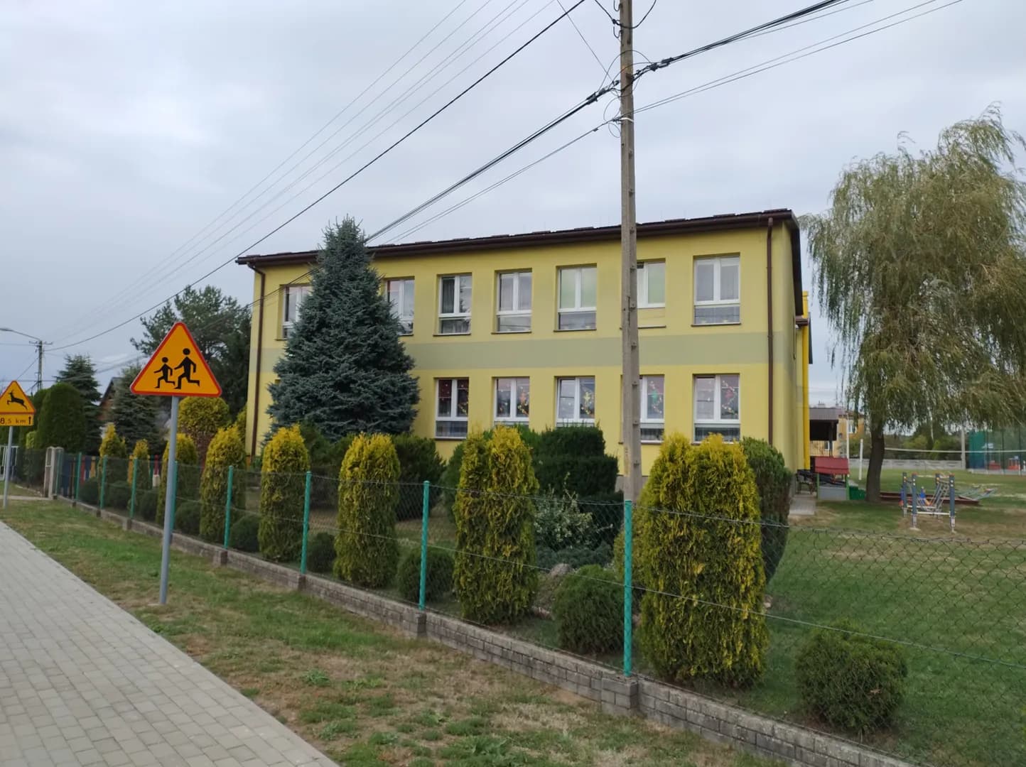 Żółty, piętrowy budynek Szkoły Podstawowej w Bukowcu widziany zza ogrodzenia.