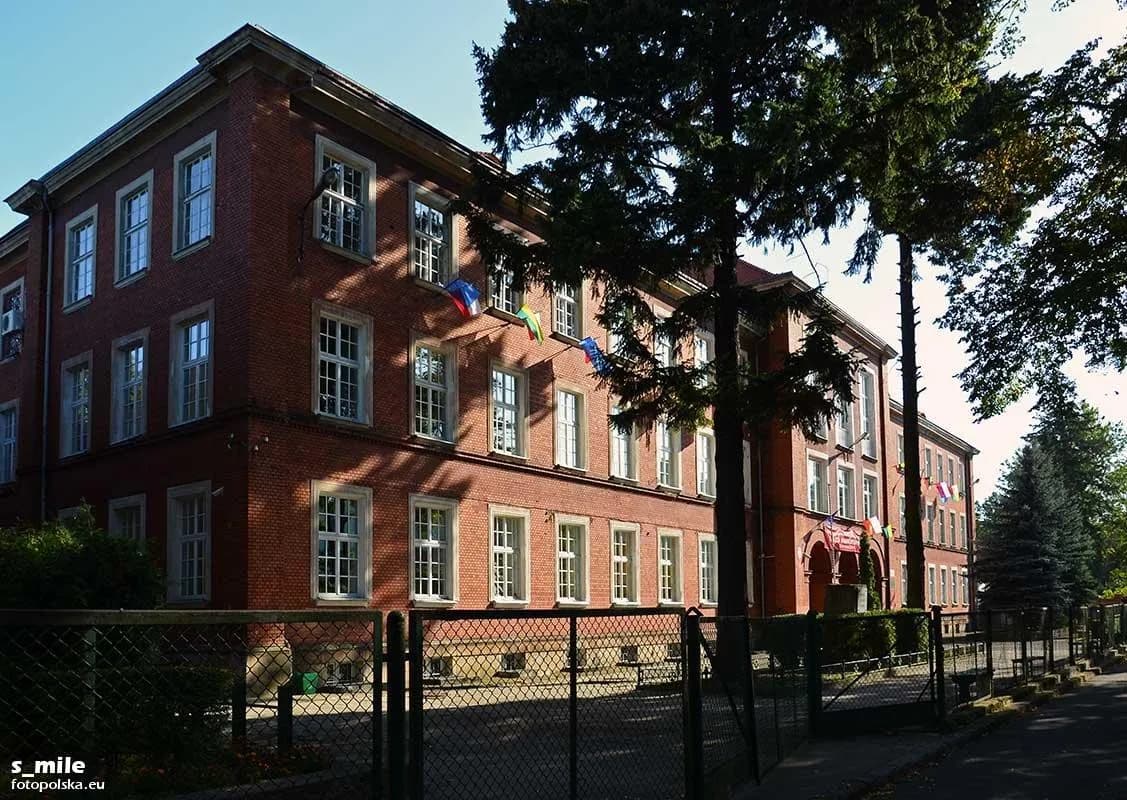 Ceglany budynek Liceum Ogólnokształcącego im. Jana Pawła II w Złotoryi widziany zza ogrodzenia