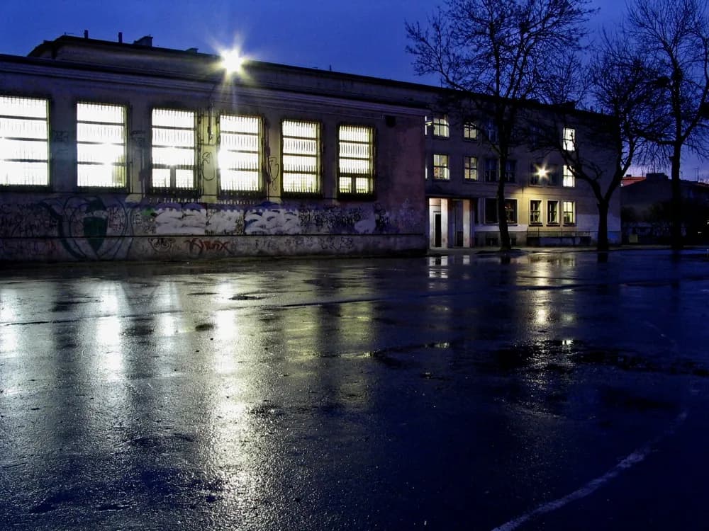 Oświetlony budynek i boisko Szkoły Podstawowej nr 91 w Łodzi nocą po deszczu