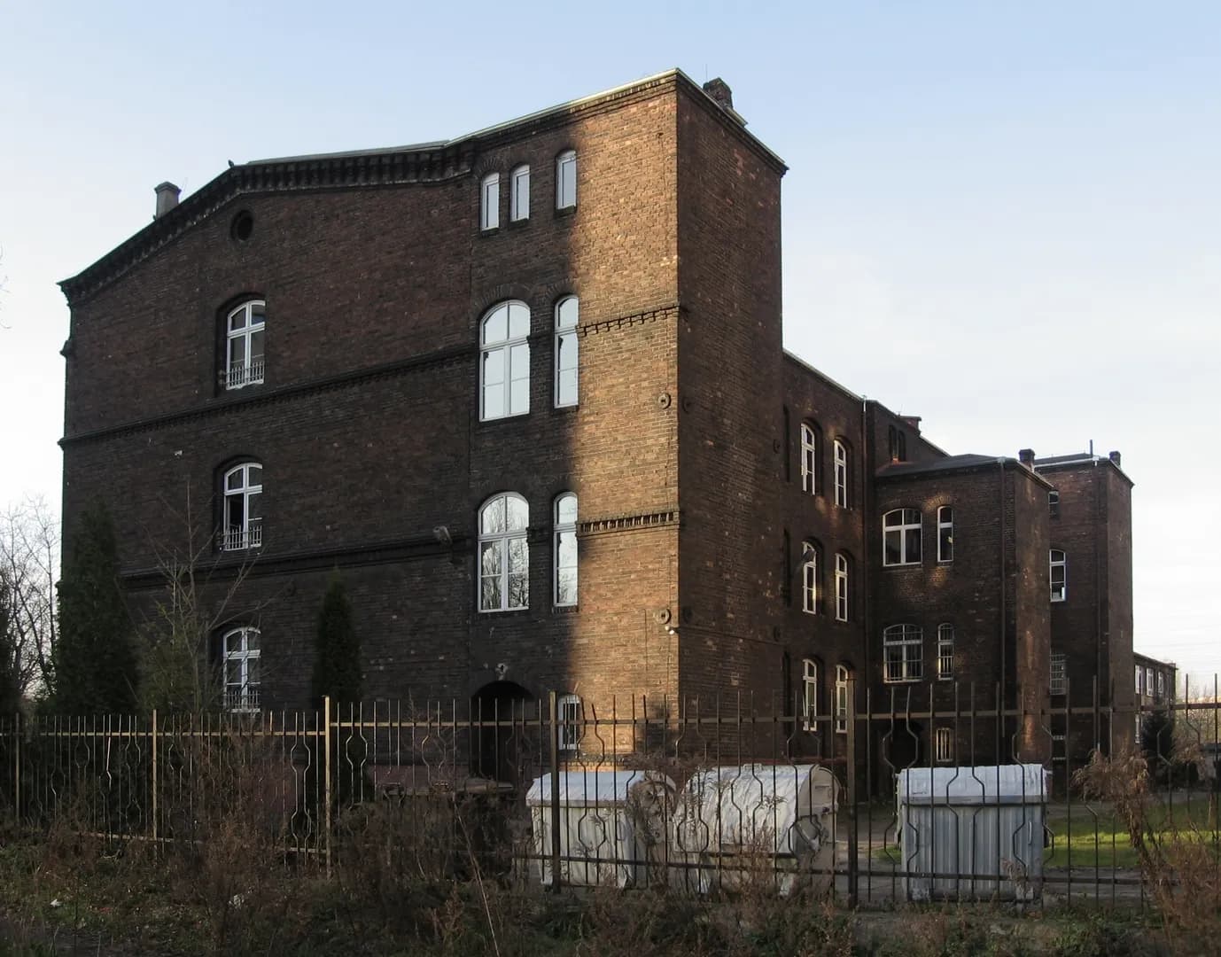 Ceglany budynek Szkoły Podstawowej nr 16 w Katowicach widoczny zza ogrodzenia.