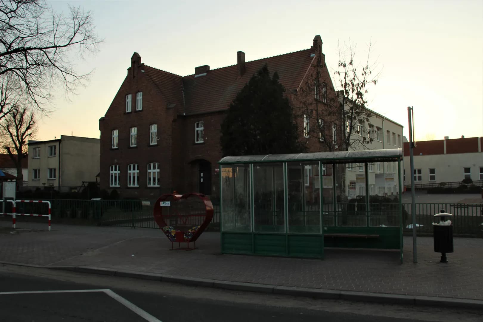 Ceglany budynek szkoły w Niepruszewie widoczny zza przystanku autobusowego