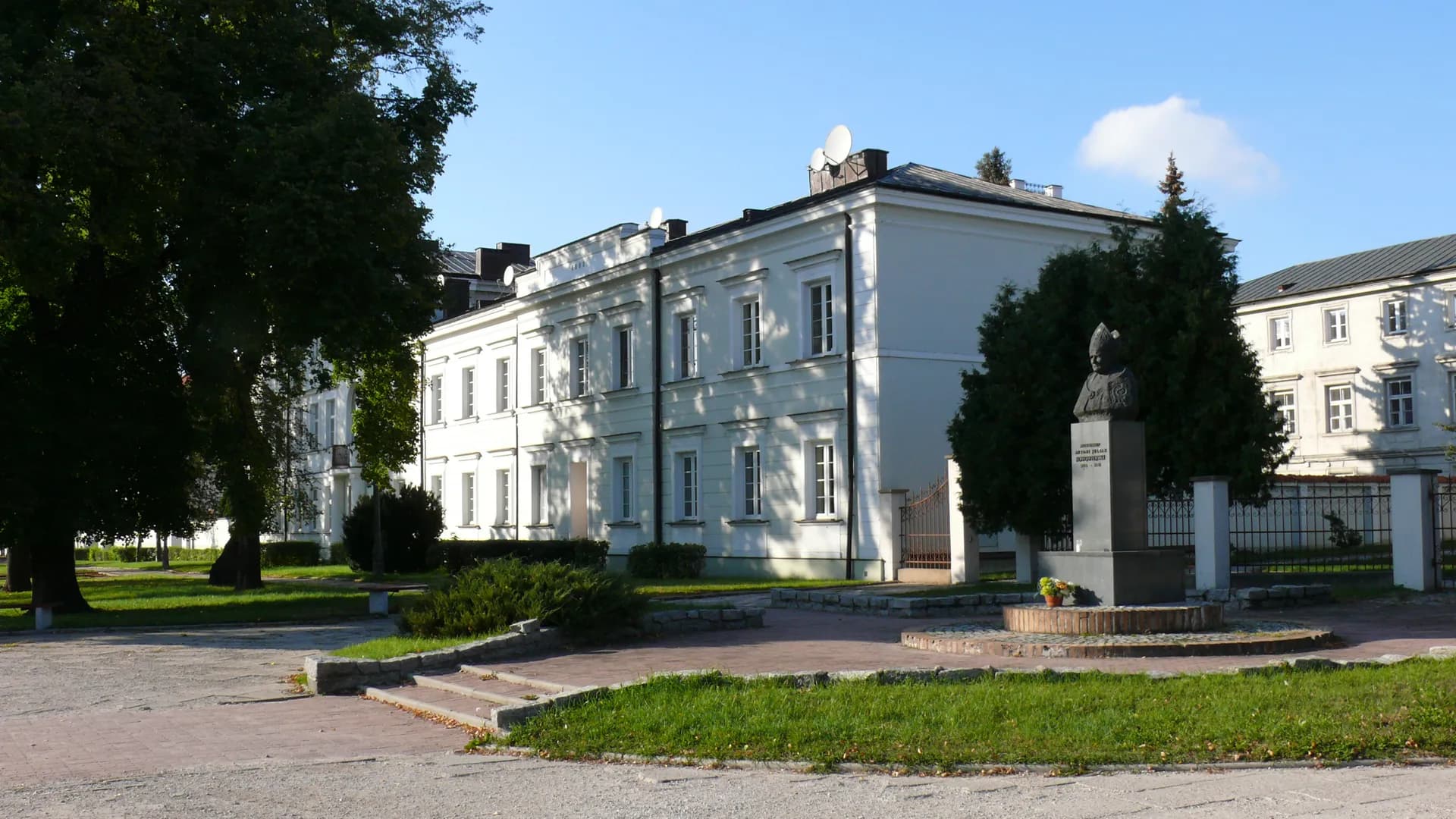 Zabytkowy budynek klasztorny i pomnik w otoczeniu zieleni w Płocku