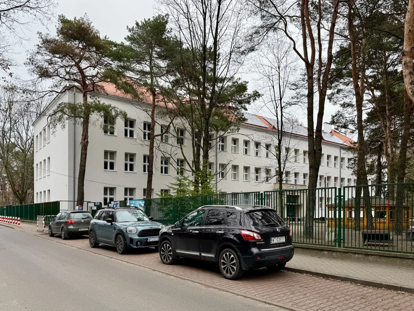 Budynek Szkoły Podstawowej nr 138 w Warszawie widoczny zza ogrodzenia i drzew