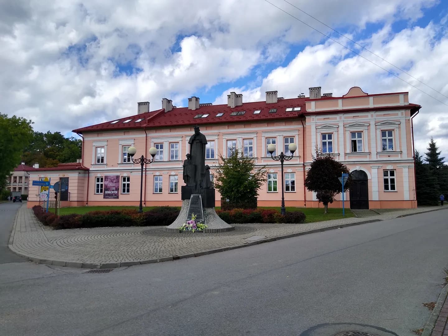 Budynek Samorządowego Liceum Ogólnokształcącego w Głogowie Małopolskim z pomnikiem na pierwszym planie