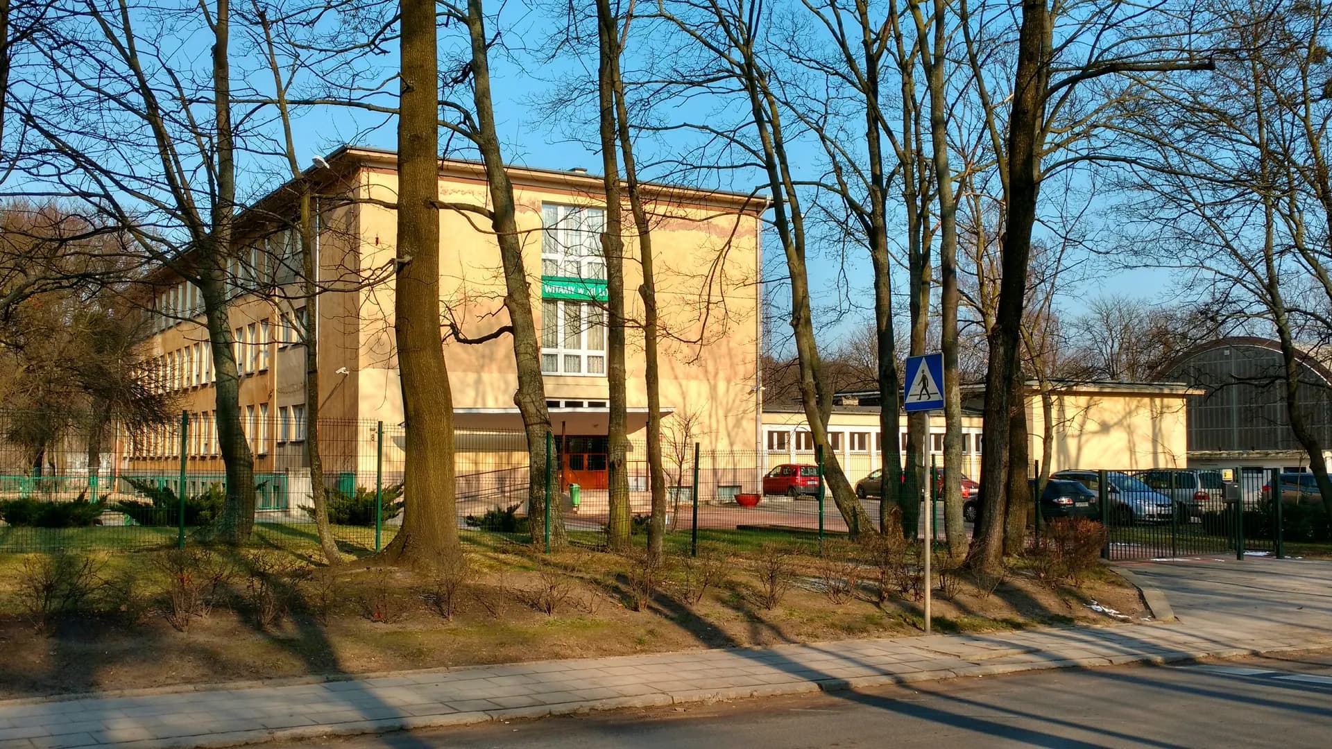 Widok na budynek XII Liceum Ogólnokształcącego w Poznaniu zza drzew