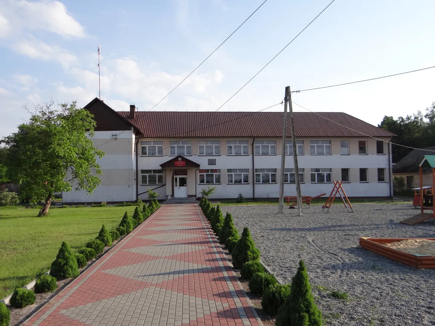 Budynek Publicznej Szkoły Podstawowej w Domostawie z chodnikiem i placem zabaw