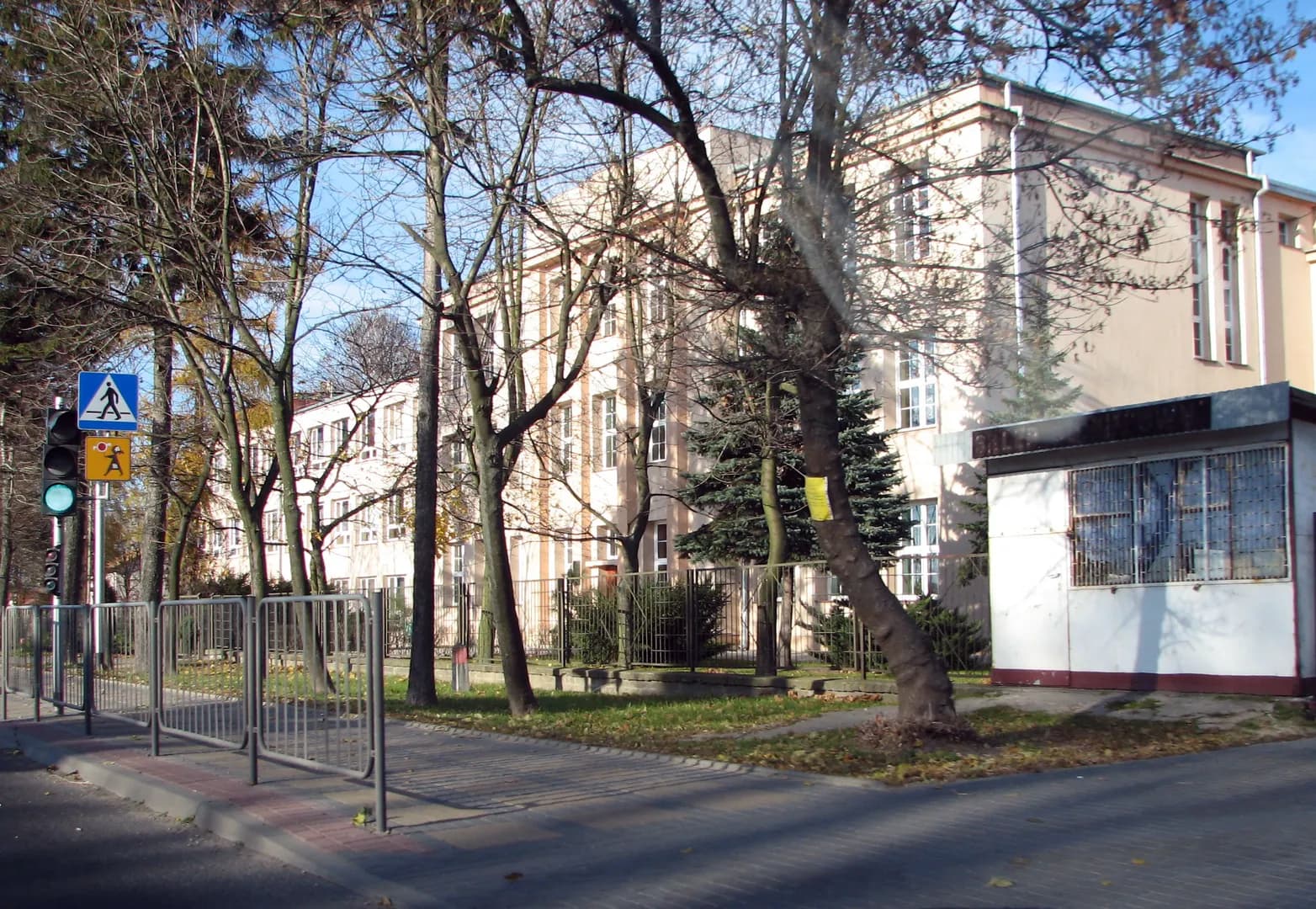 Budynek Szkoły Podstawowej w Jastkowie widziany zza drzew i ogrodzenia
