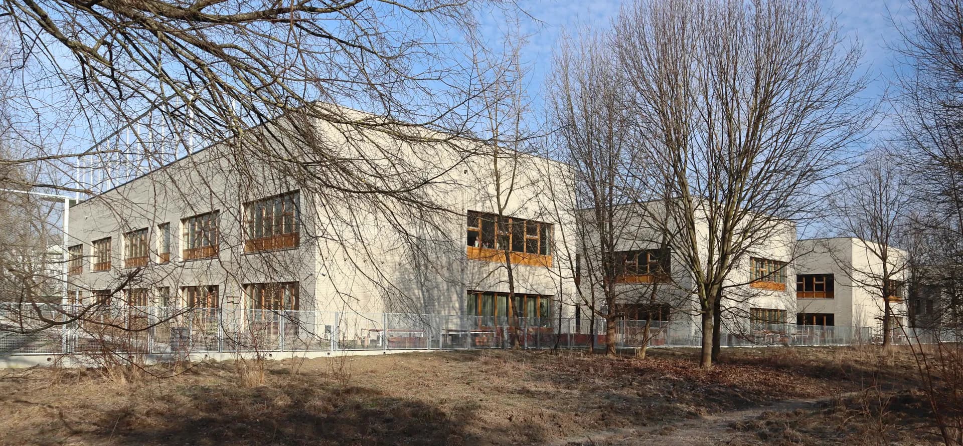 Nowoczesny budynek Szkoły Podstawowej nr 406 w Warszawie widoczny zza drzew