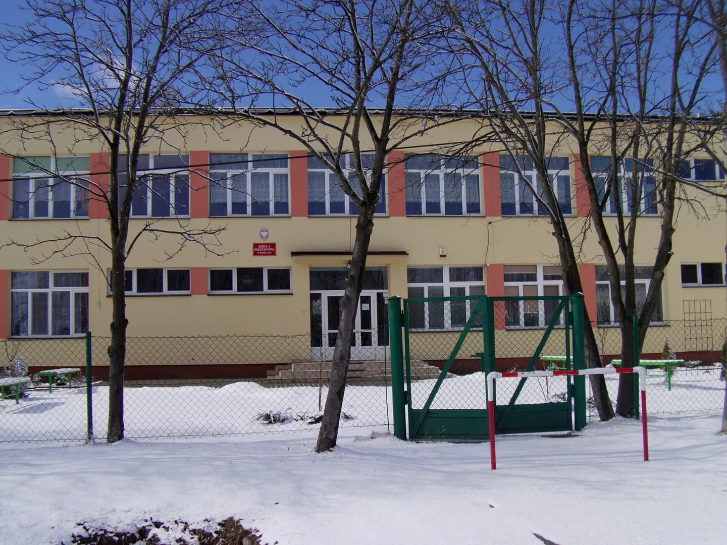 Elewacja Szkoły Podstawowej w Boreczku zimą, widok zza ogrodzenia