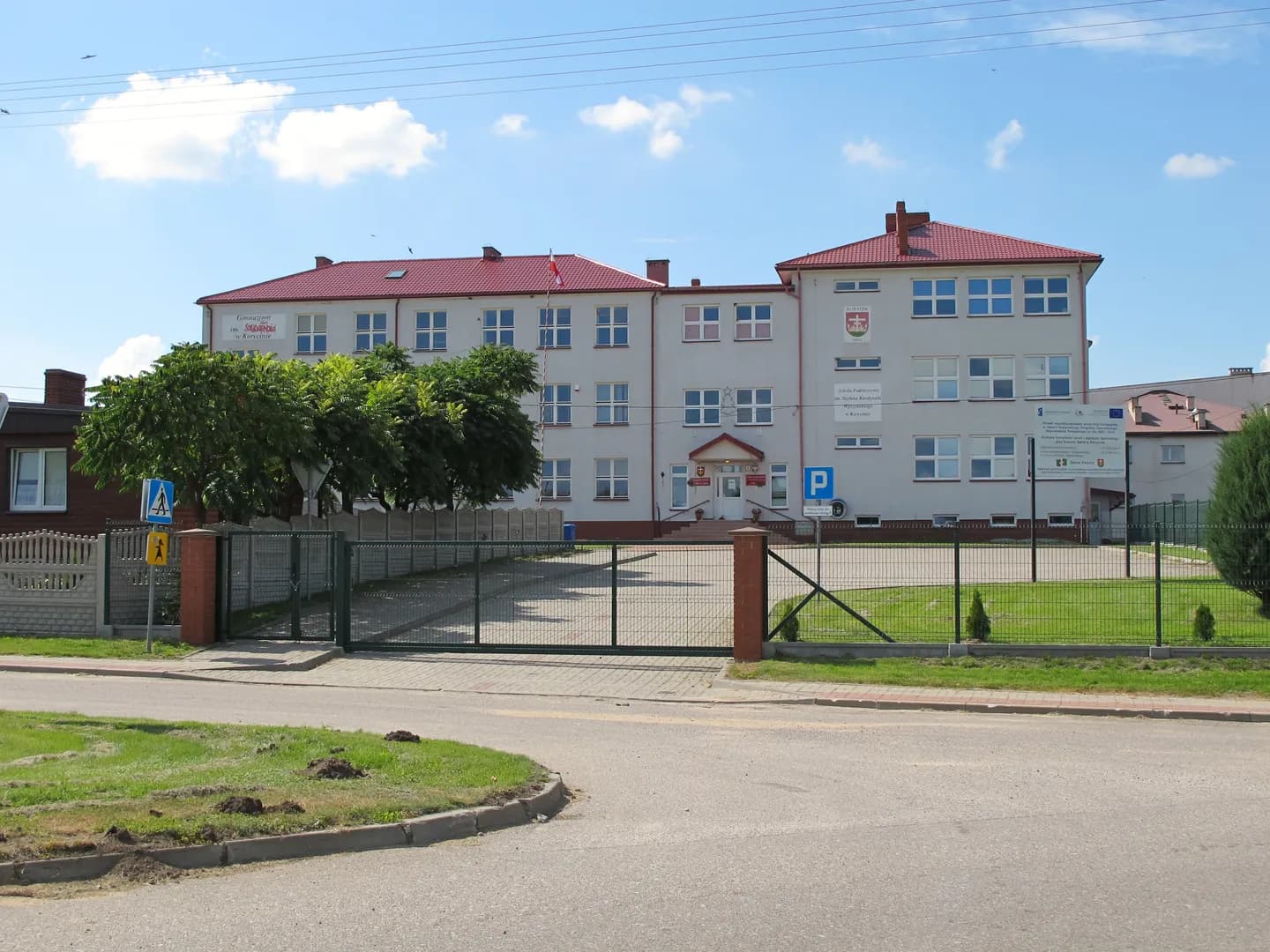 Fasada budynku Szkoły Podstawowej w Korycinie z ogrodzeniem i bramą wjazdową