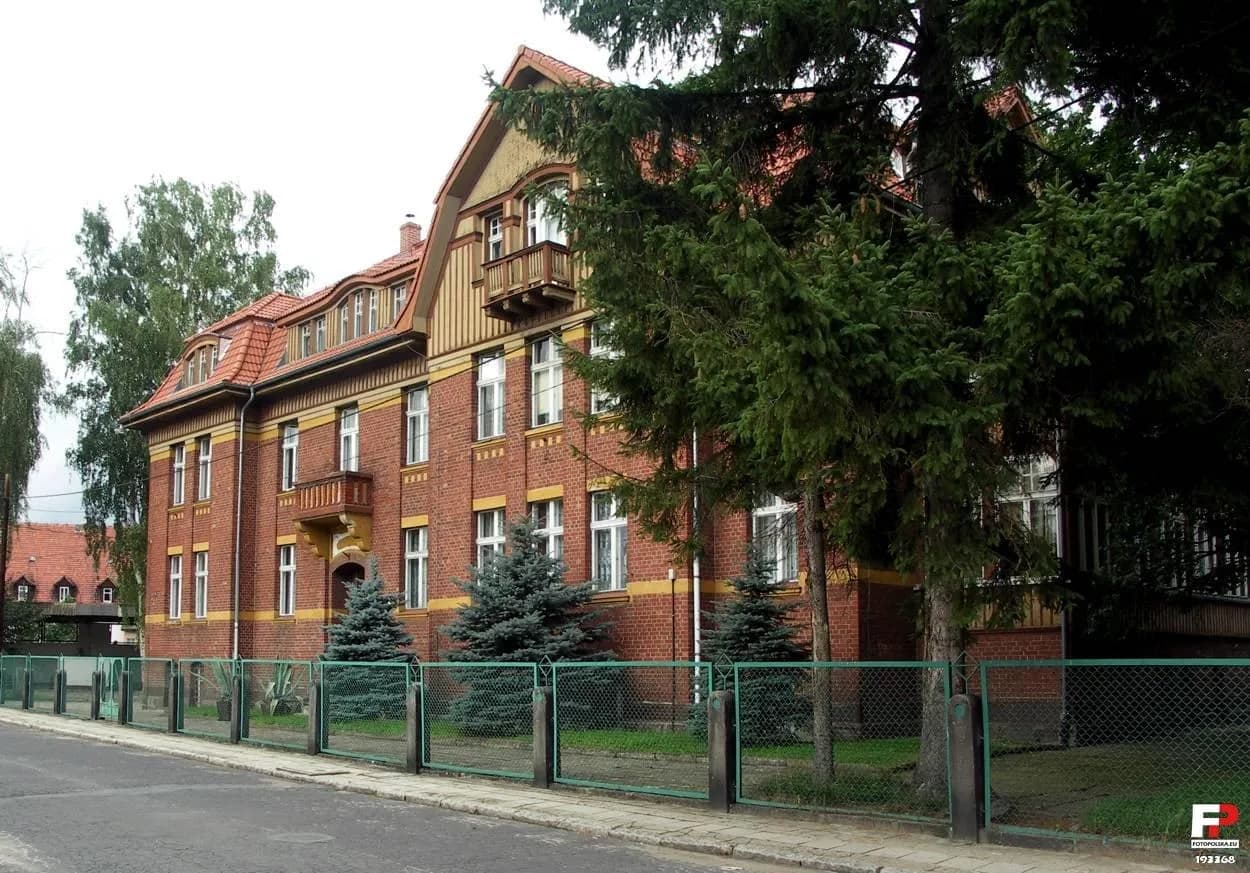 Ceglany budynek Młodzieżowego Ośrodka Socjoterapii w Jeleniej Górze widziany zza ogrodzenia